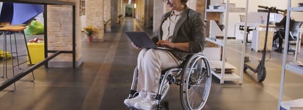 Person in wheelchair with laptop within a large office.