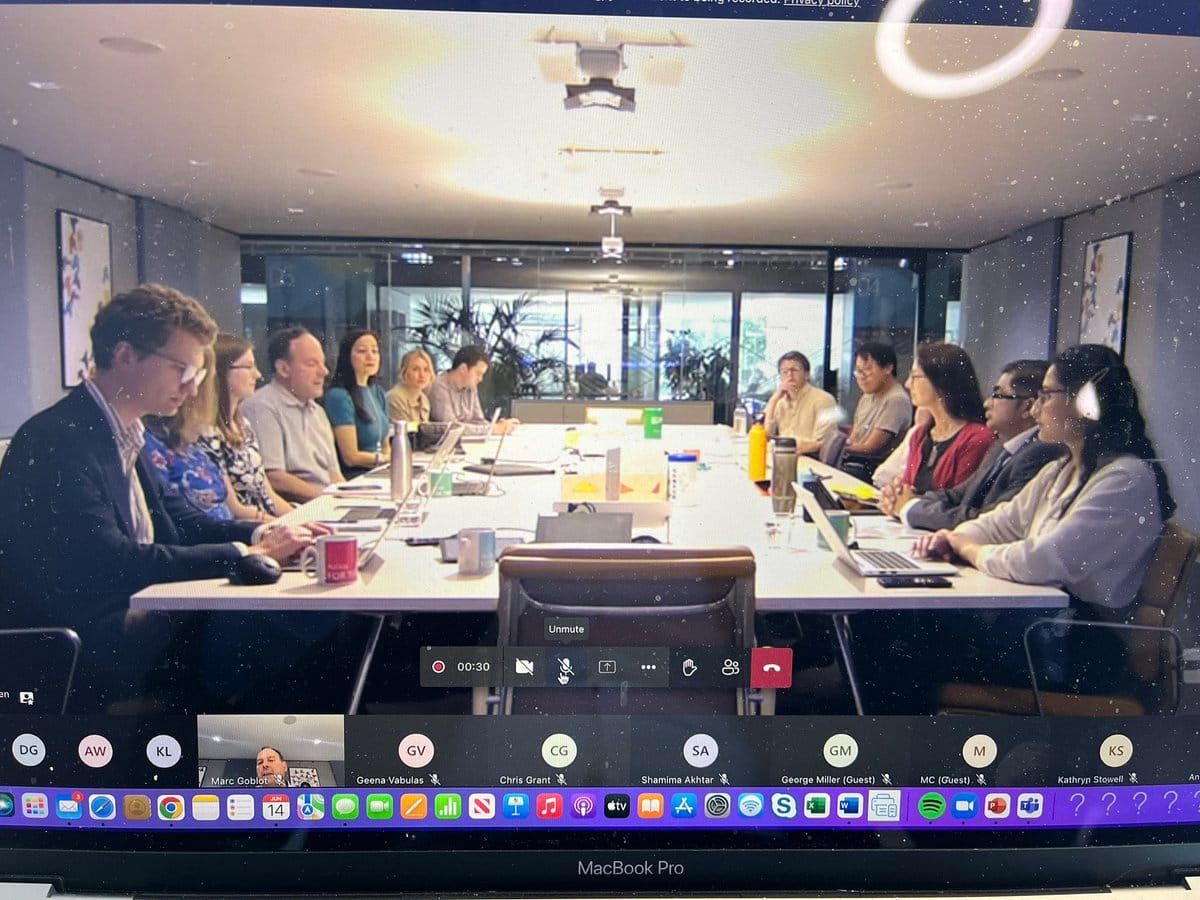 A computer screen showing a Zoom meeting with a large table circled by people in discussion.